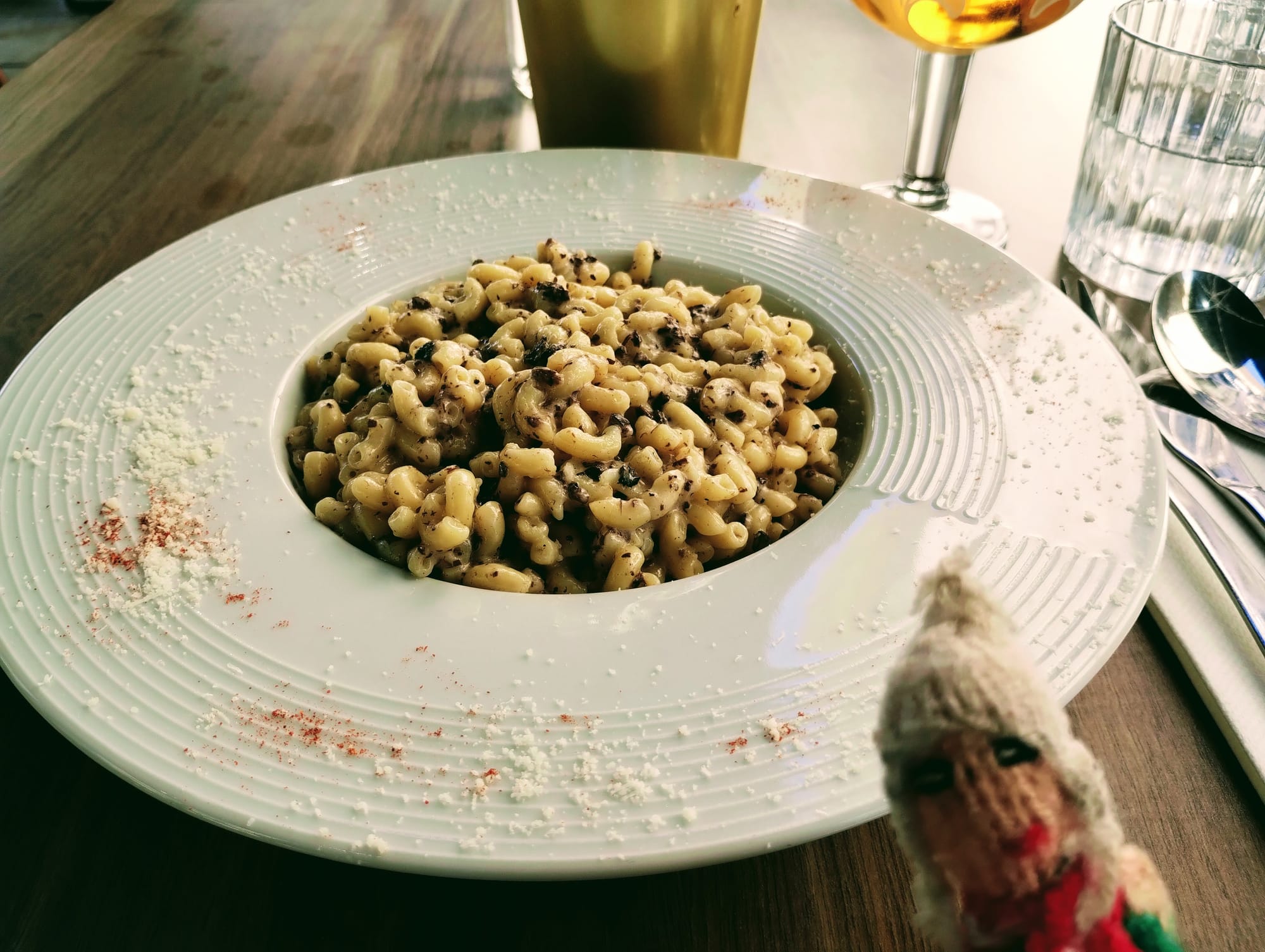 A photograph of the finger puppet in front of a large dish of small pasta with truffles and parmesan.