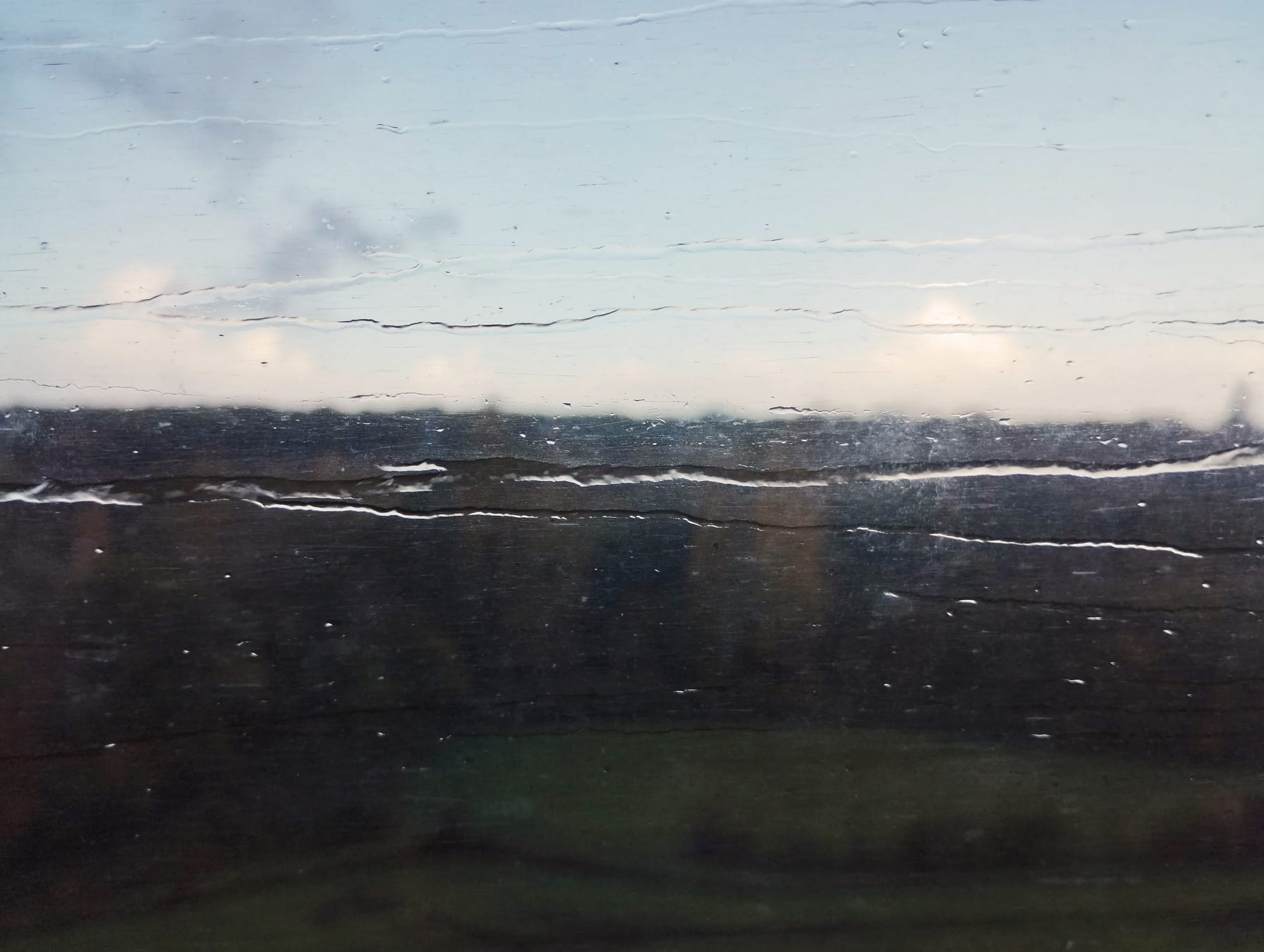 View through a rain-streaked window with a blurred dark landscape and sky visible.