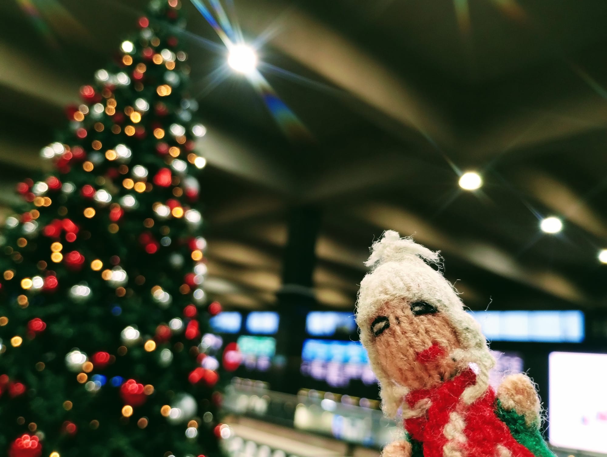 A perkily festive Peruvian finger puppet in front of a blurred Christmas tree with red, white, and gold lights.