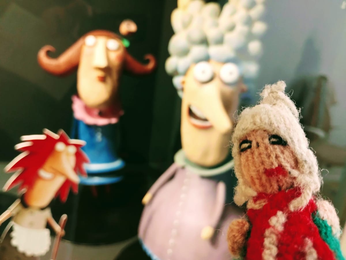 Finger puppet among his kind; an elderly woman in a red and green shawl, a smiling woman with large white hair, and another with spiky red hair.