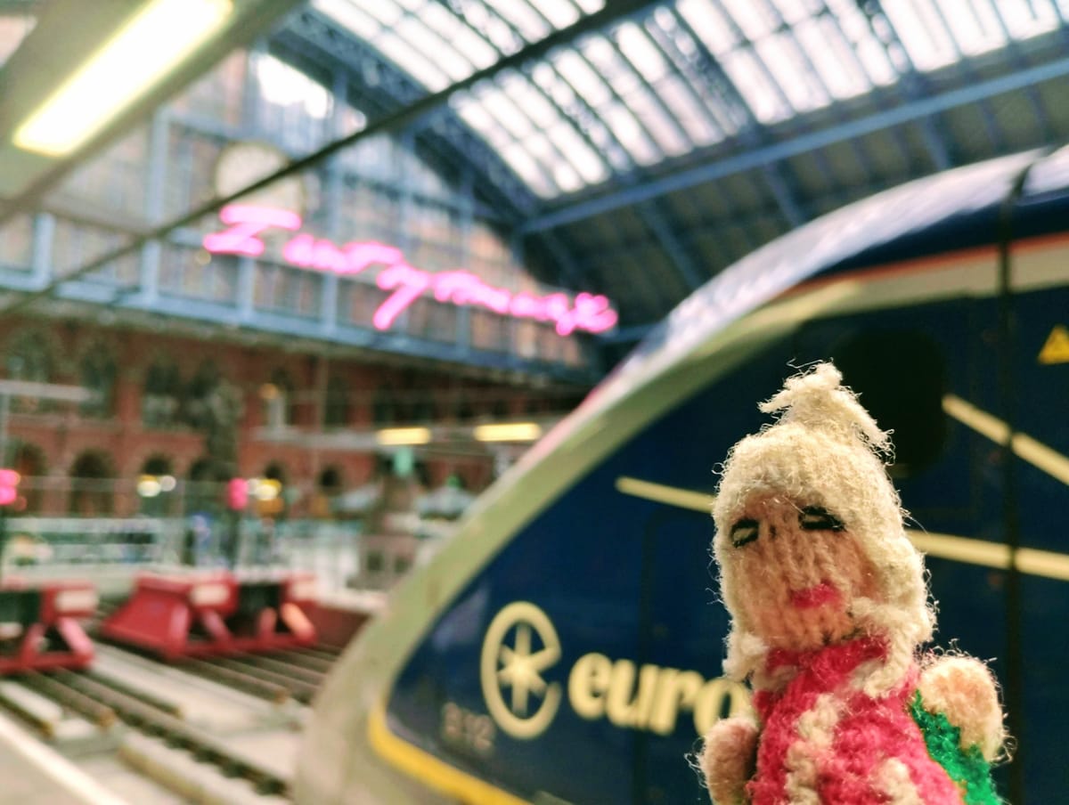 Close-up shot of a Peruvian finger puppet in front of a Eurostar train under the arched roof of London Saint Pancras International.