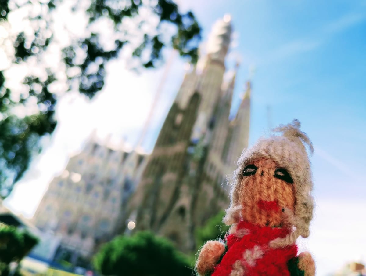 Close-up of a Peruvian finger puppet in front of the Sagrada Família Cathedral in Barcelona, Spain, on a sunny day.